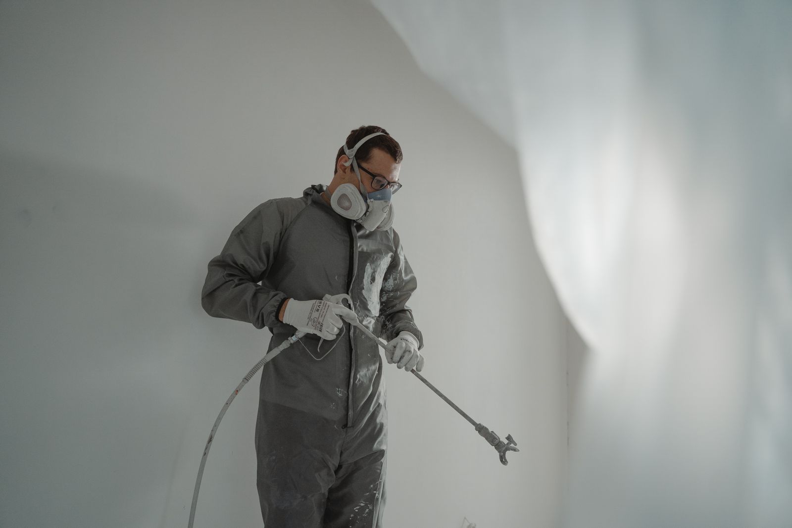 A professional painter spray-finishing the walls of a new-construction interior